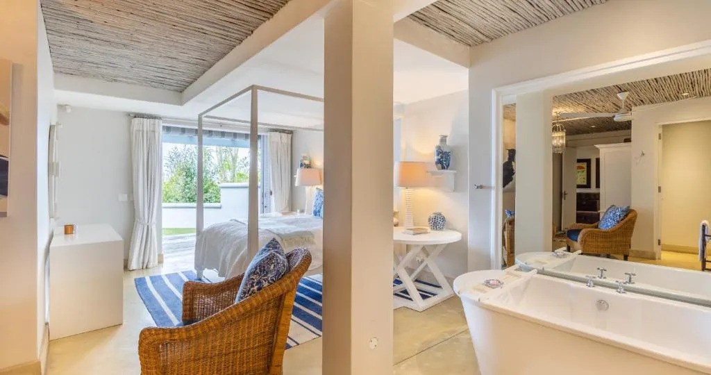 Freestanding bathtub beside a four-poster bedroom, thatch ceiling above