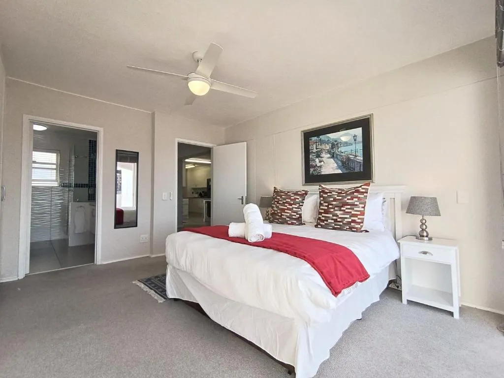 Bedroom with a ceiling fan, red throw and doors opening to an ensuite bathroom and kitchen
