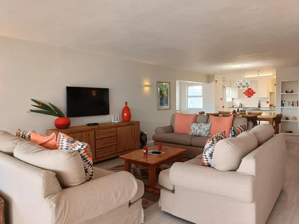 Open-plan lounge with two beige sofas, a wooden TV console and a dining area beyond