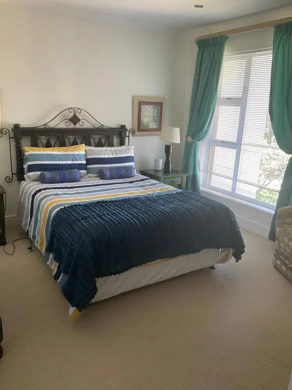 Bedroom with a wrought-iron headboard, striped bedding and a garden-facing window