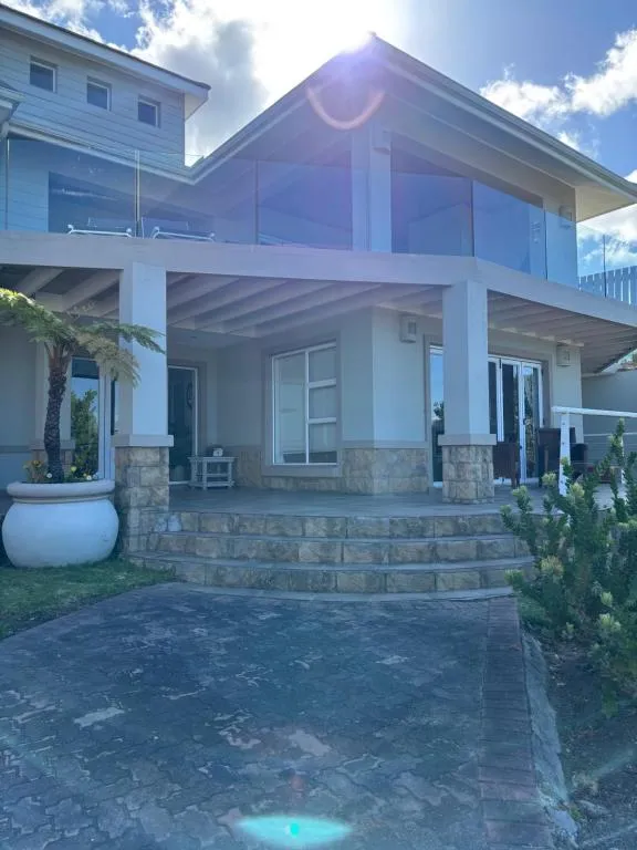 Double-storey stone and glass guesthouse exterior with an upper balcony and paved driveway