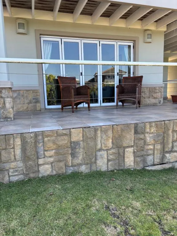 Paved terrace with wicker armchairs above a stacked-stone retaining wall and a lawn strip