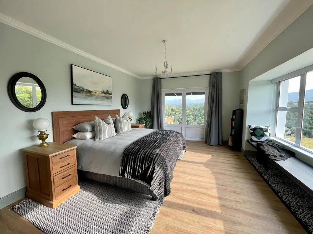 Bedroom with a wooden bed and doors onto a balcony overlooking forested hills and mountains