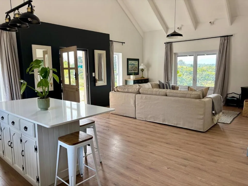 Open-plan kitchen island and lounge under a vaulted, beamed ceiling with a view over the valley
