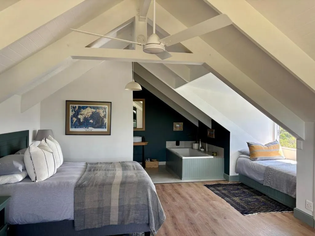 Loft bedroom under exposed beams with two beds and a freestanding bath built into the eaves