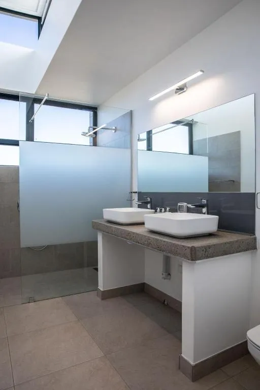 Bathroom with twin vessel sinks, a frosted-glass walk-in shower and a large skylight
