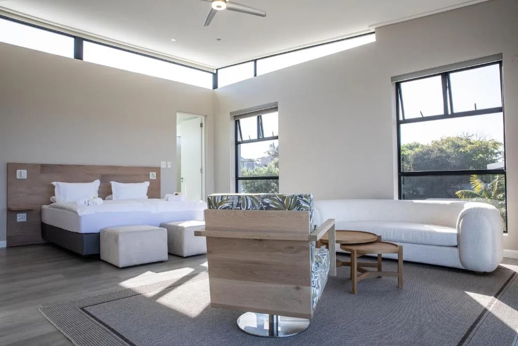Bedroom with a wood-panelled headboard, ceiling fan and large windows onto greenery