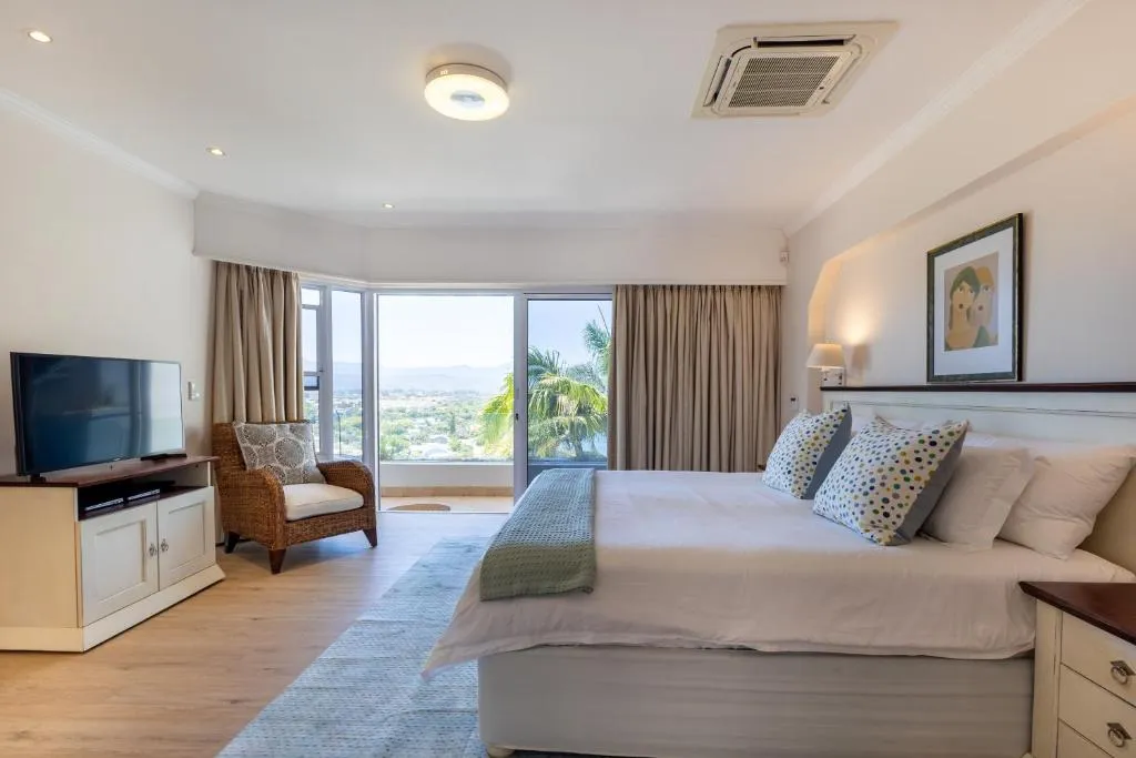 Bedroom with a wicker armchair and sliding doors onto a balcony overlooking hills and rooftops