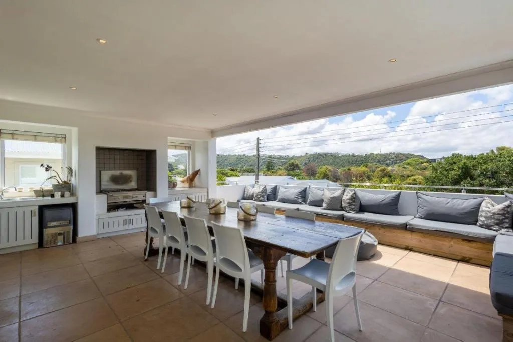 Covered outdoor patio with a built-in braai, TV niche and long dining table facing the hills
