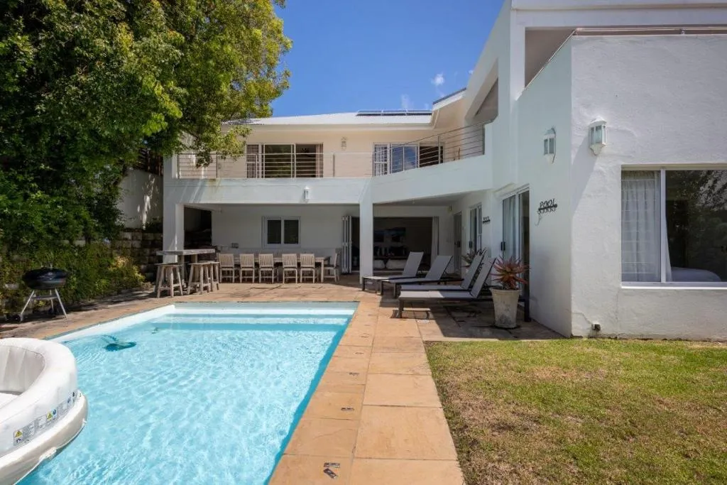 Swimming pool with loungers, a kettle braai and the house's covered patio beyond