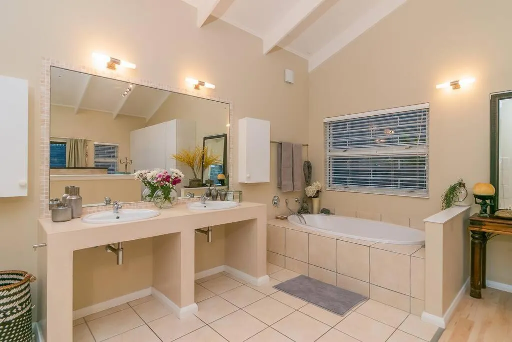 Bathroom with a double vanity, freestanding-style bath, and a tiled window with wooden blinds