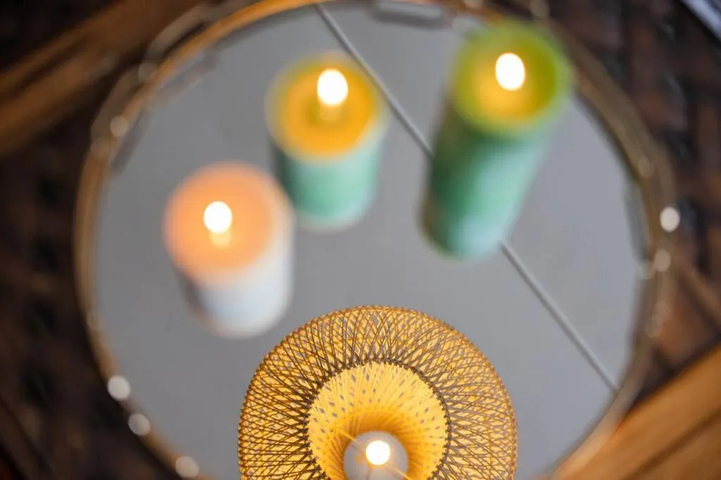 Close-up of lit candles on a mirrored tray beside a woven pendant lamp