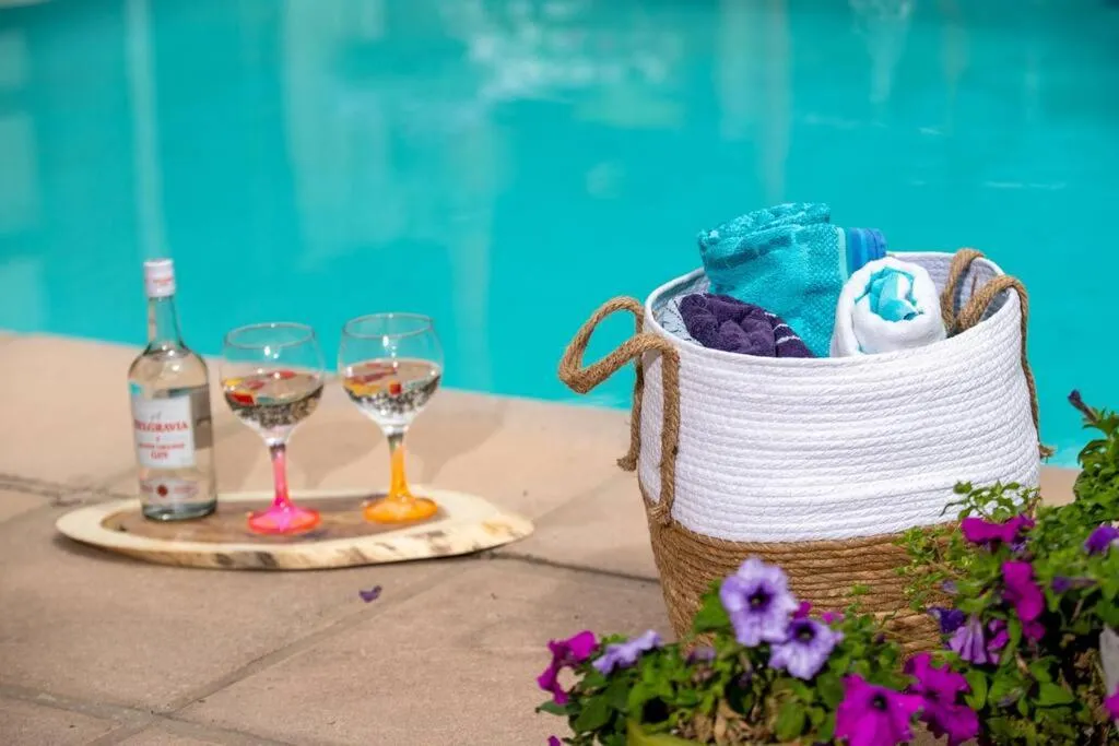 Poolside styling shot with a gin bottle, two glasses, and a towel basket beside the water