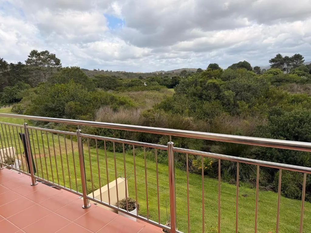 Balcony with terracotta tiles and steel railing overlooking a lawn and dense bush