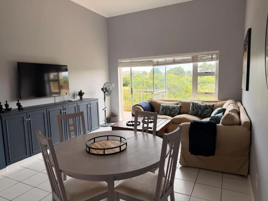 Open-plan lounge and dining area with a corner couch and a view over green treetops