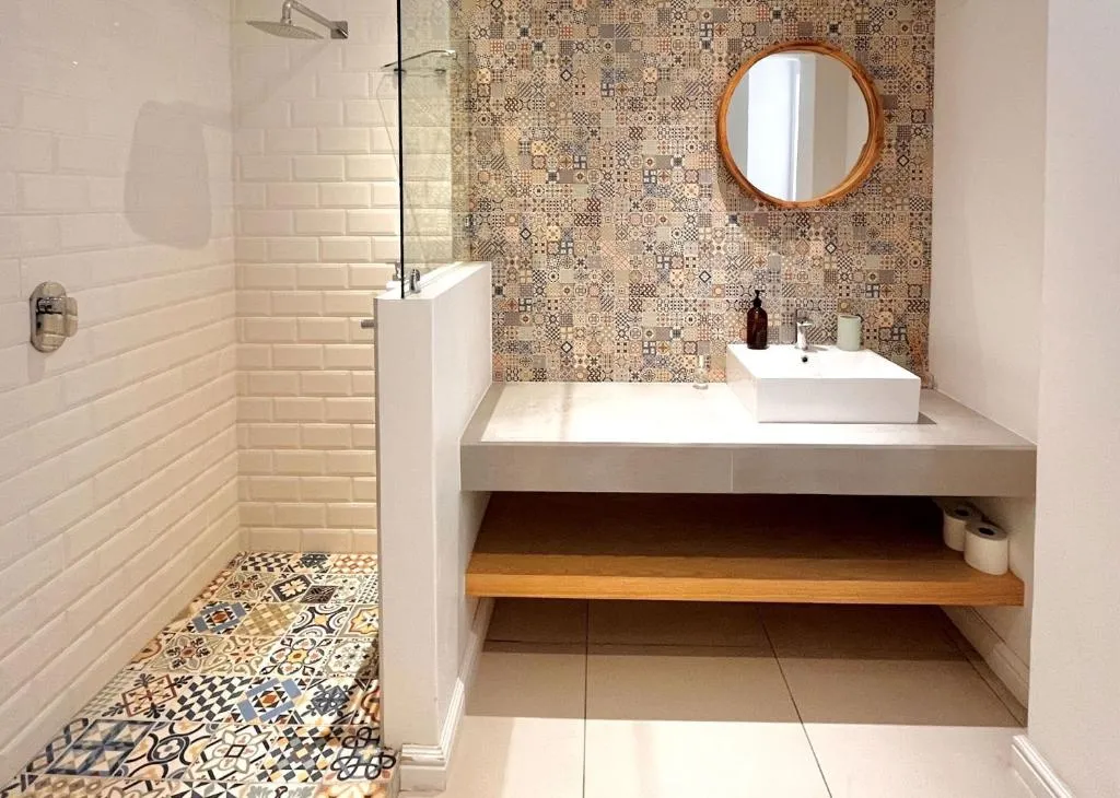 Bathroom with a walk-in shower, patterned tile floor and a round mirror over a floating vanity