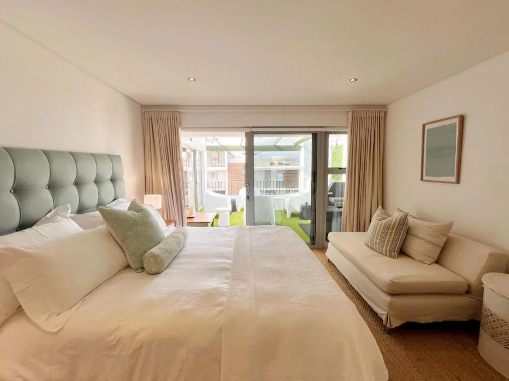 Bedroom with a padded headboard and sliding doors onto an artificial-turf balcony