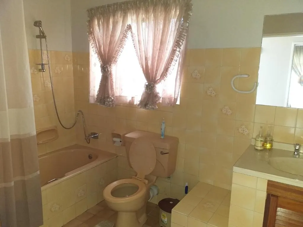 Bathroom with yellow tile, corner bath, curtained window and pedestal sink