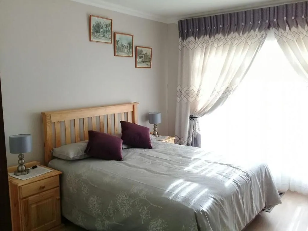 Bedroom with pine headboard, patterned curtains and framed village prints above the bed