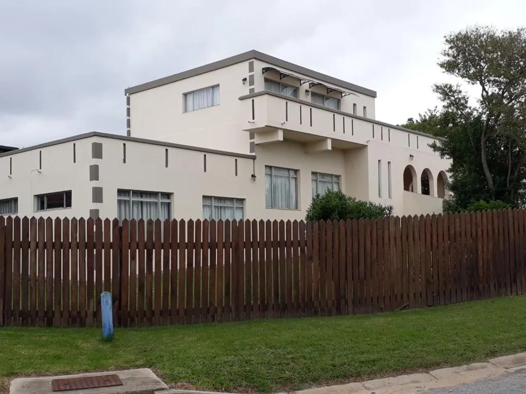 Cream double-storey guesthouse behind a wooden picket fence with an arched veranda