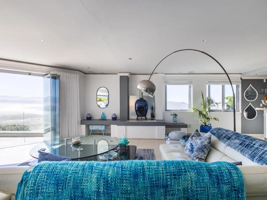 Lounge with a blue ceramic wood-burner stove and floor-to-ceiling windows onto the ocean