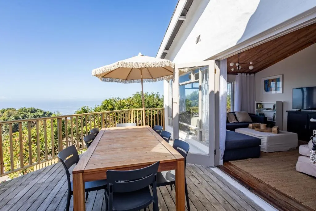 Wooden deck with an umbrella-shaded dining table and a clear sea view over the treeline