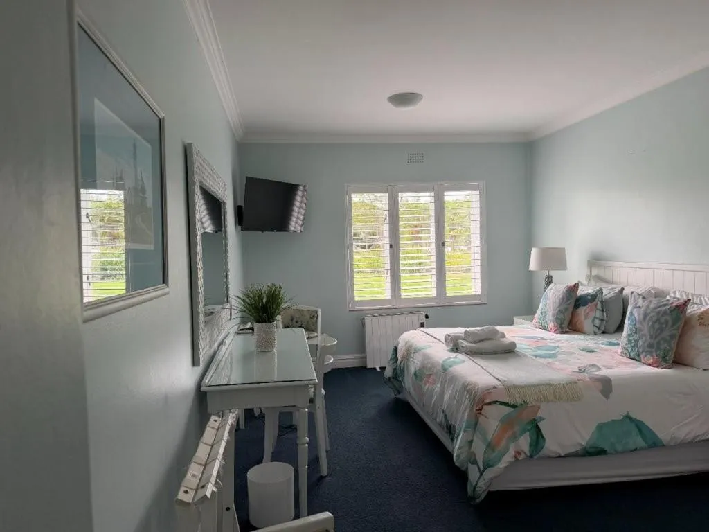 Bedroom with pastel walls, floral bedding and plantation shutters onto a garden view