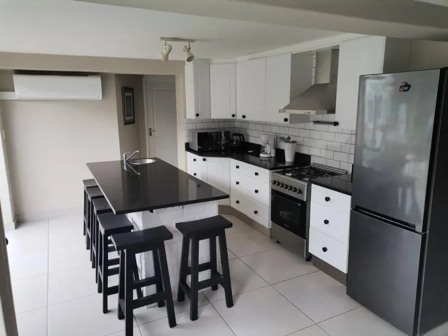 Kitchen with a black-topped island, bar stools, white cabinetry, and a wall-mounted air conditioner