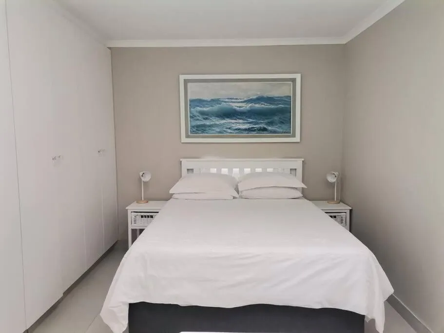 Bedroom with white double bed, built-in wardrobes, and a framed seascape above the headboard