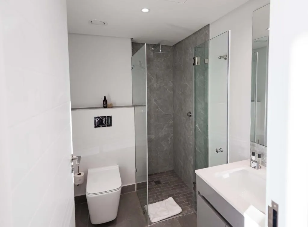 Bathroom with a glass-walled shower, dark tile and a floating white vanity