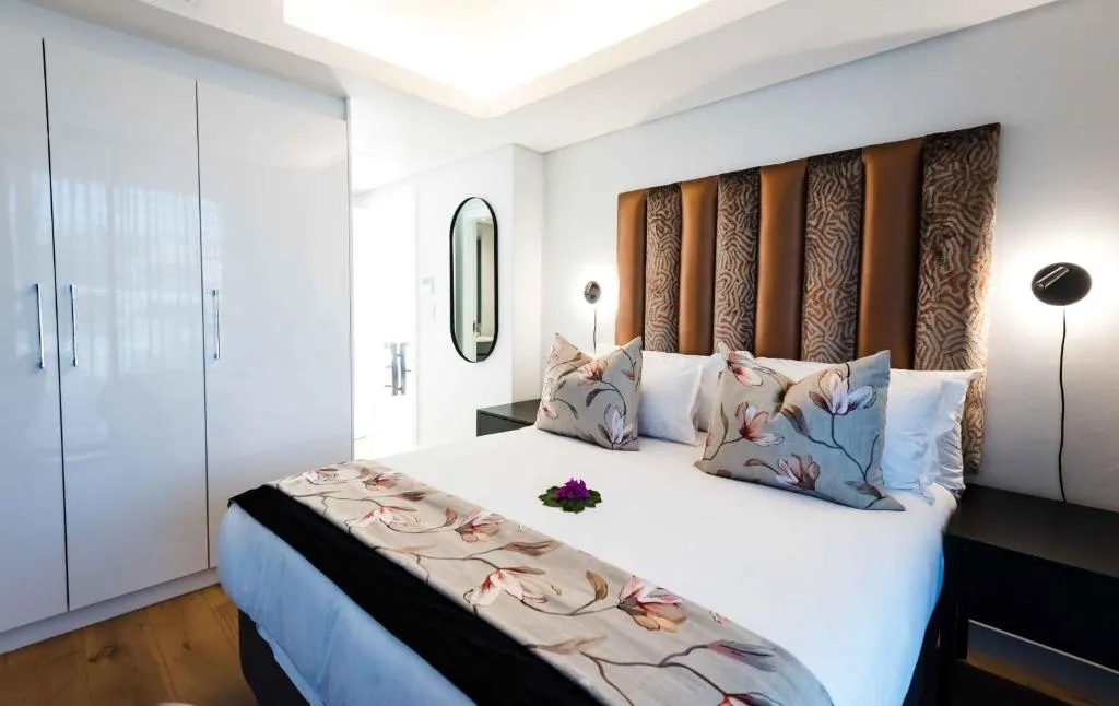 Bedroom with a glossy white wardrobe, bronze textured headboard and floral cushions