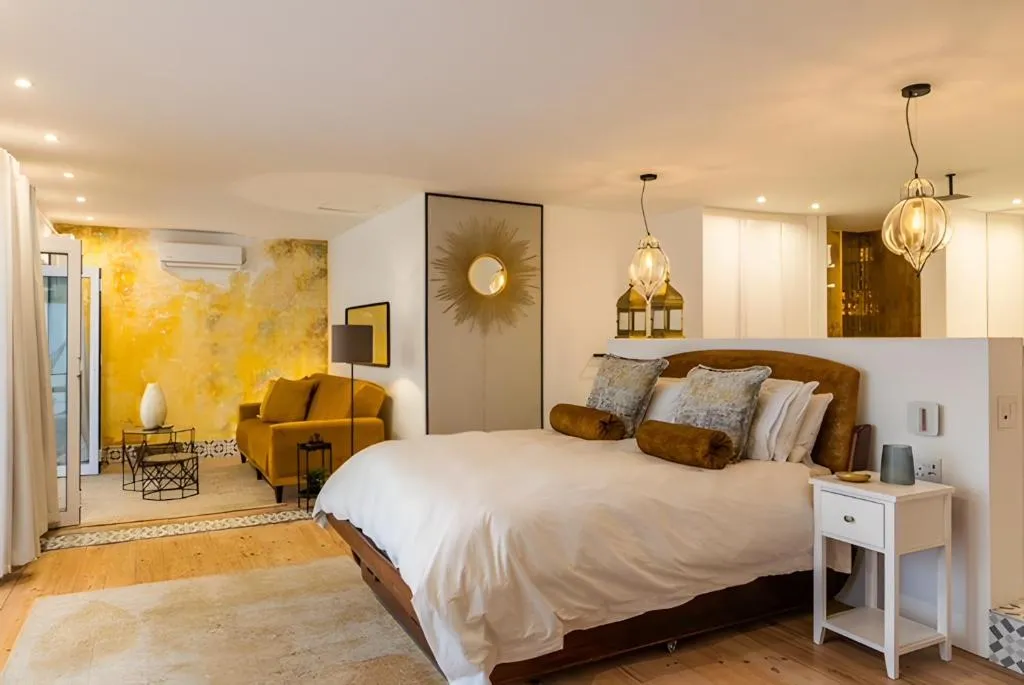 Studio bedroom with a mustard accent wall, sunburst mirror, and wall-mounted air conditioner
