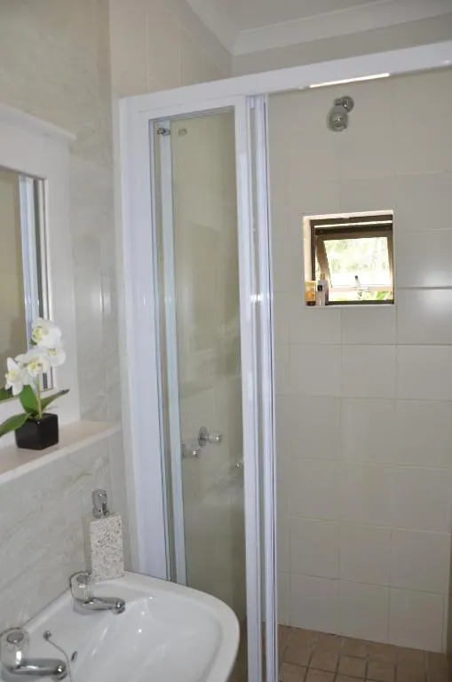 En-suite bathroom with a glass-enclosed corner shower and pedestal basin below a window