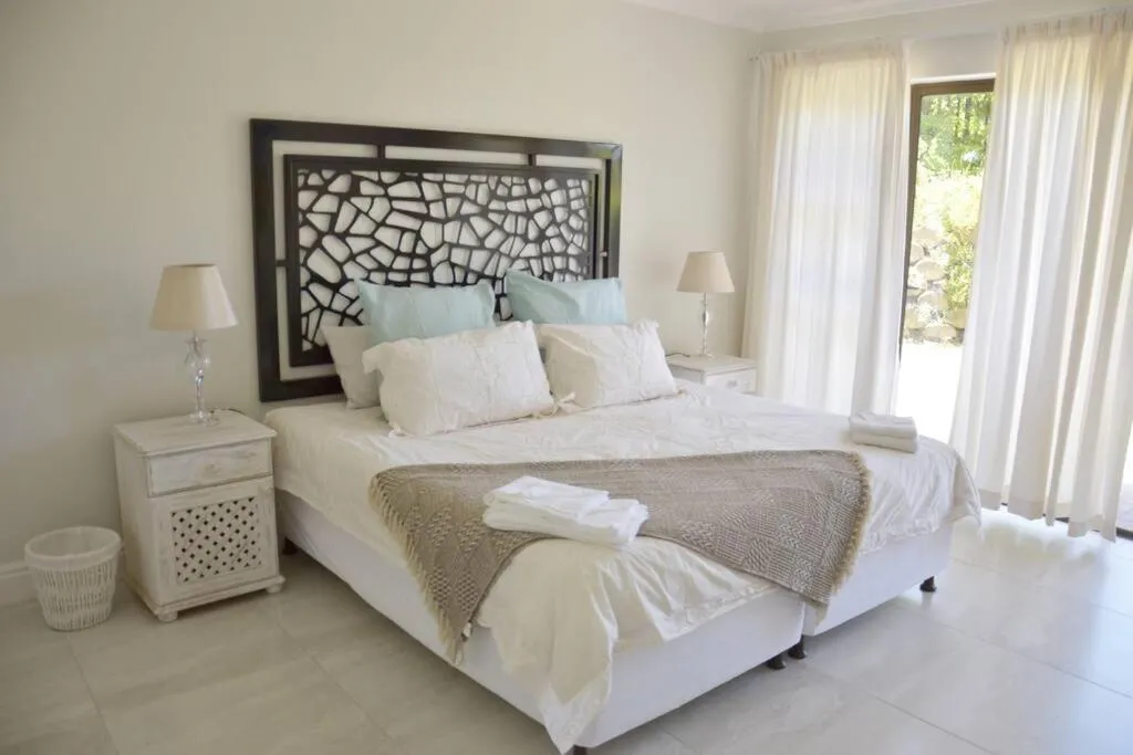 Bedroom with white linen, patterned headboard, and curtained doors opening onto the garden