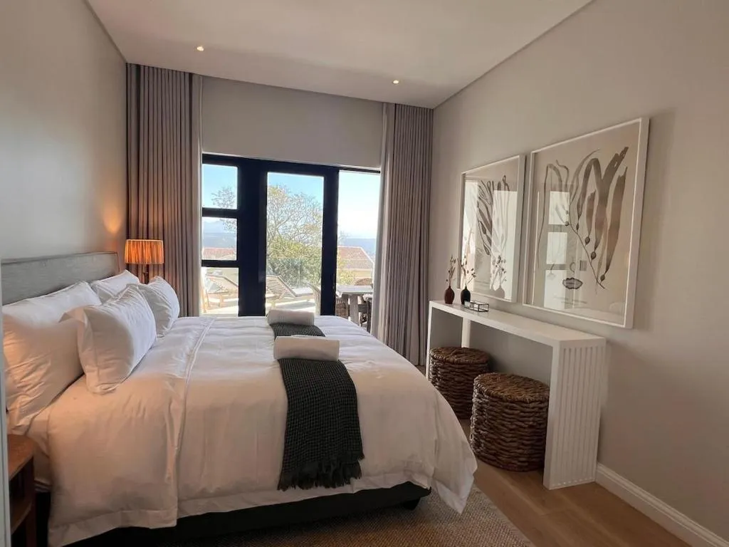 Bedroom with upholstered headboard, layered white linen, and glass doors opening onto a balcony