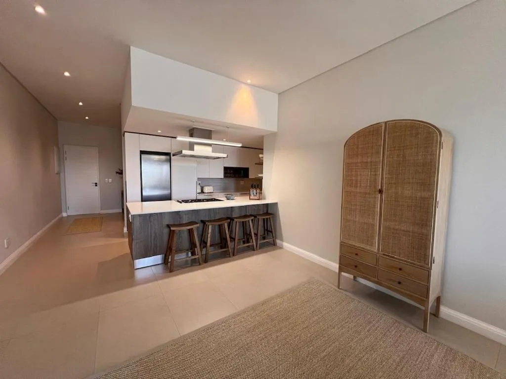 Open-plan kitchen with a two-tone island, bar stools, and a tall rattan-fronted cabinet
