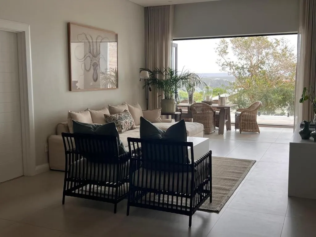 Open-plan living room with folding doors onto a balcony overlooking treetops and hazy hills