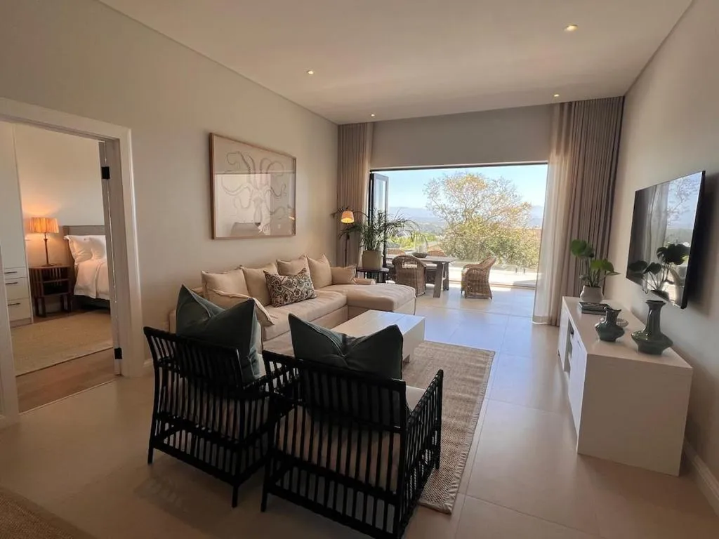 Living room sofa and armchairs facing a folding glass door onto the balcony, TV console alongside