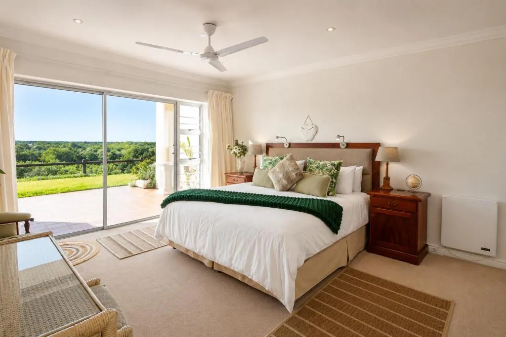 Bedroom with sliding doors onto a private balcony overlooking a lawned garden and tree line
