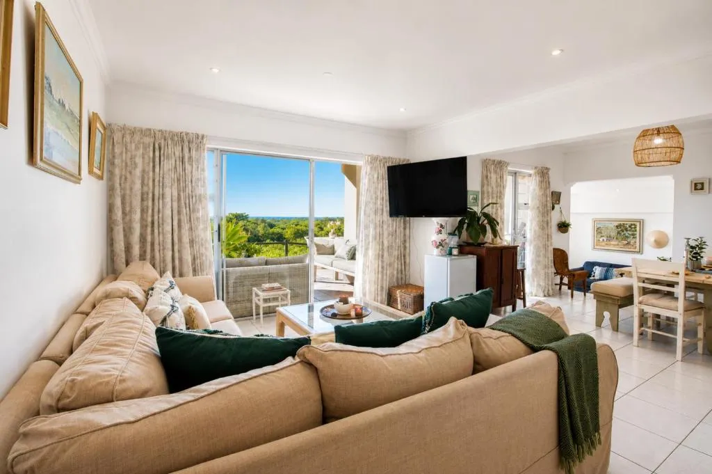Open-plan living room with a sectional couch, TV and sliding doors onto a balcony over the treetops