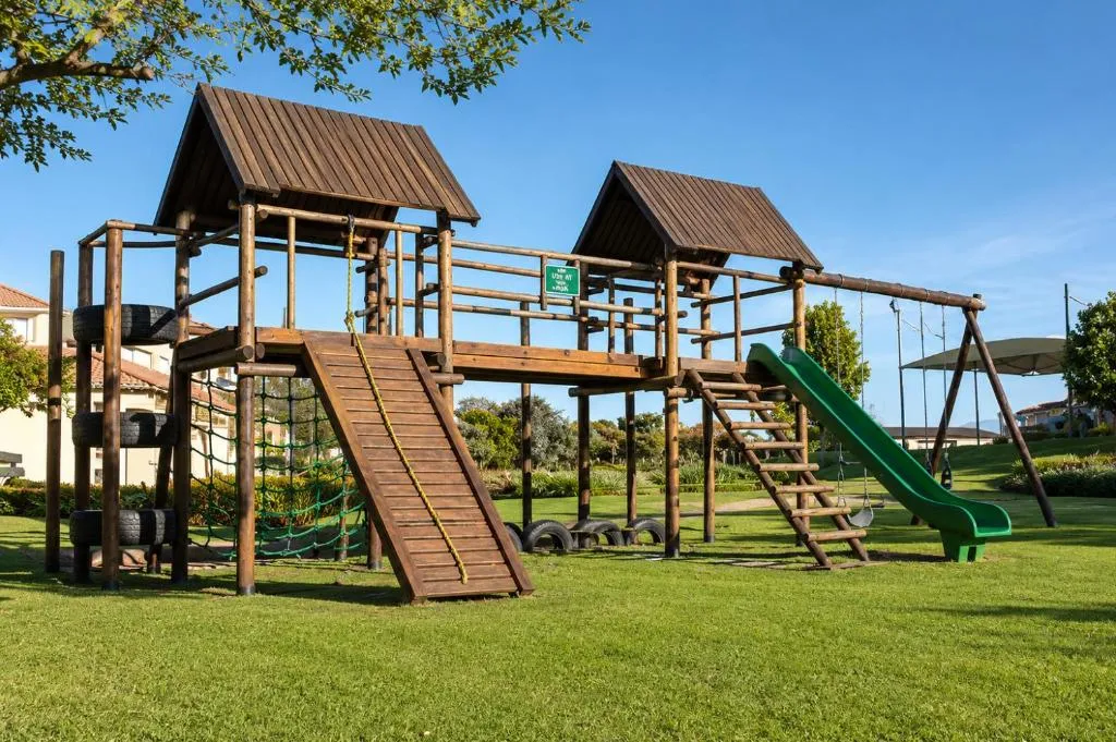 Wooden jungle gym with a slide, swings and tyre climbing wall on the estate's communal lawn