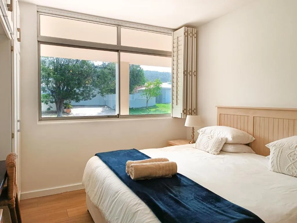 Bedroom with a large window looking onto a leafy garden and neighbouring rooftops