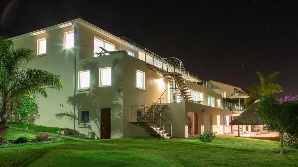Night view of the guesthouse exterior with lit windows, staircase, pool and lawn