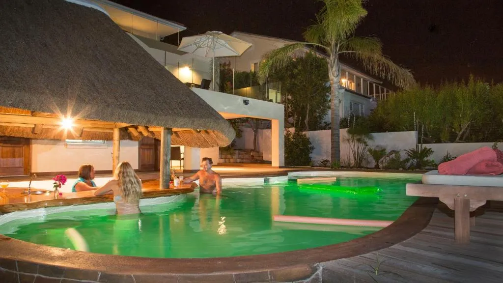 Guests in the outdoor pool lit green at night beside the thatched bar