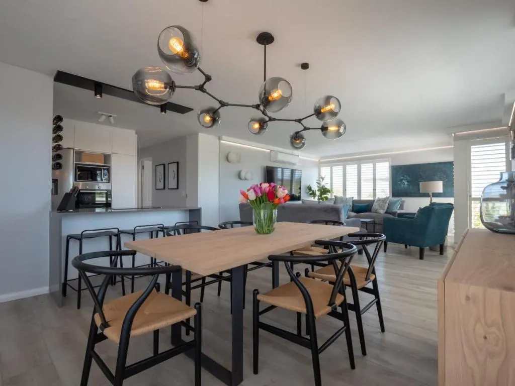 Open-plan dining area beneath a sculptural pendant light, with the kitchen and lounge beyond
