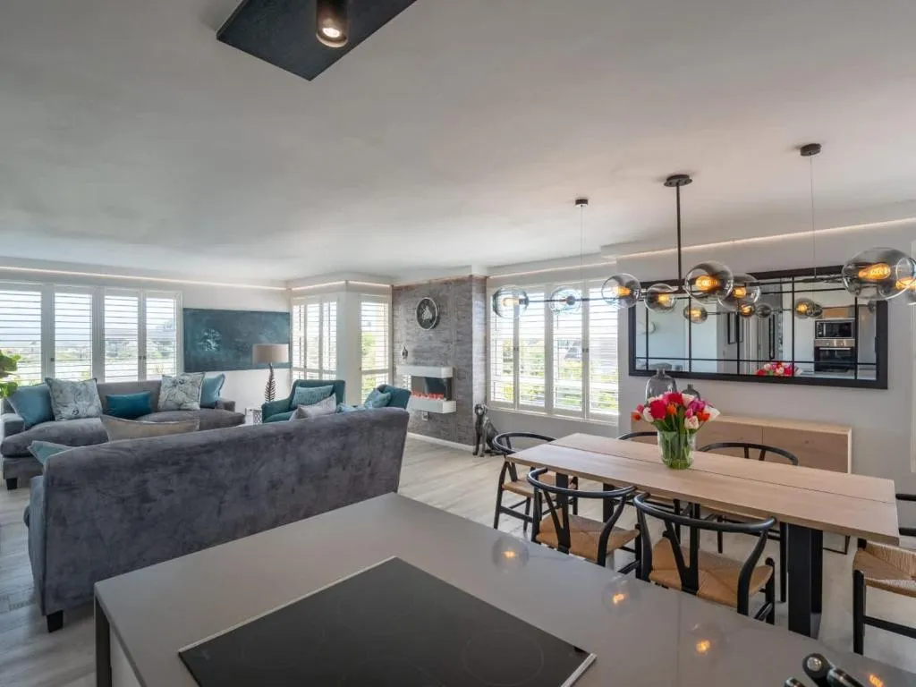Open-plan living area with a built-in fireplace, plantation shutters and a dining table beyond
