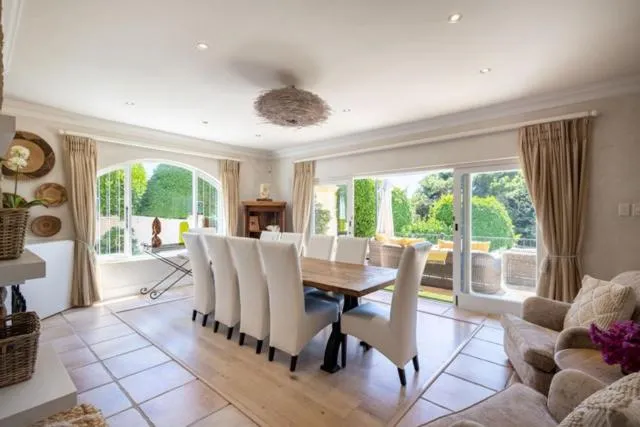 Dining room seating ten guests with tall arched windows opening onto a landscaped garden
