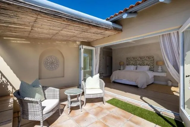 Covered patio with wicker armchairs beside an open-plan bedroom through sliding doors