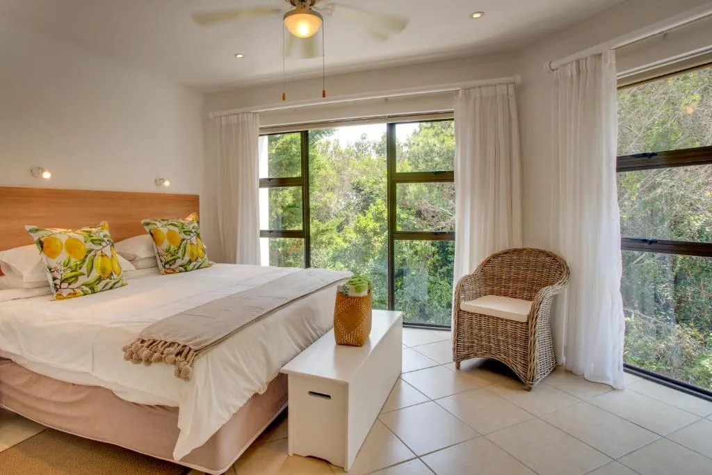 Bedroom with white linen, lemon-print cushions and floor-to-ceiling windows onto trees