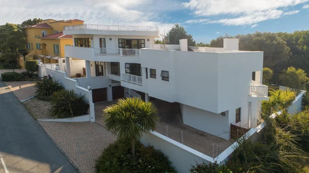Modern white multi-storey building with stacked balconies, garage and paved driveway